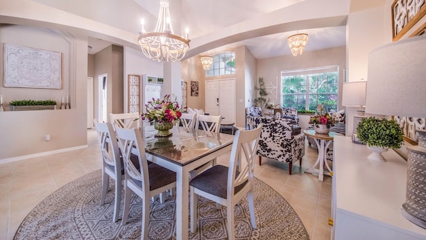Un vaste espace dédié à la salle à manger, avec une grande table et des chaises, de magnifiques lustres et une vue sur l’extérieur.