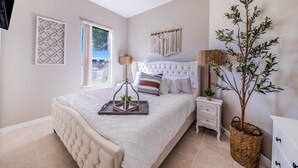 Une chambre à coucher avec un grand lit, une table de chevet, une lampe, un élément décoratif mural et une plante en pot.