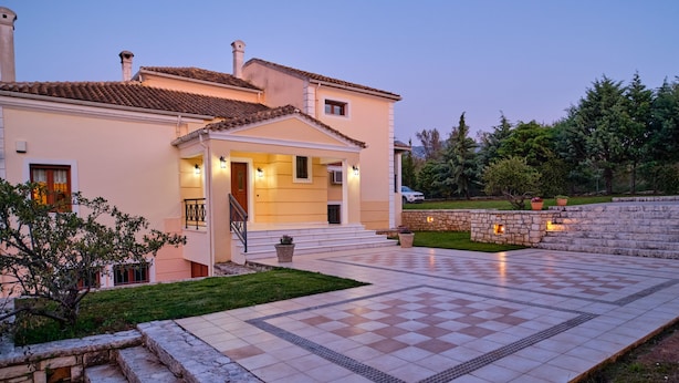Una casa de dos pisos con un patio empedrado, un muro de piedra y un pequeño jardín.