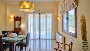 Comedor con mesa de vidrio, sillas, una araña y vistas a través de cortinas traslúcidas.