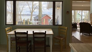 Un comedor con una mesa y sillas, un ventanal con vistas a un lago y edificios, y piso de madera.