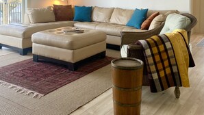 Una sala moderna con un sofá color beige, un reposapiés y un barril de madera.