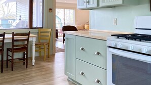 Una cocina con estufa blanca, armarios verdes y una zona de comedor con sillas y mesa de madera.