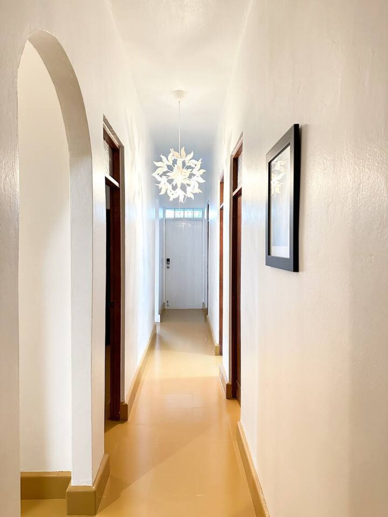 En gang med hvide vægge, trædøre, et hvidt loft og en hængende lampe.