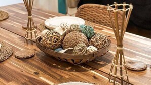 A wooden dining table with woven placemats, a bowl of decorative items, and two candle holders.