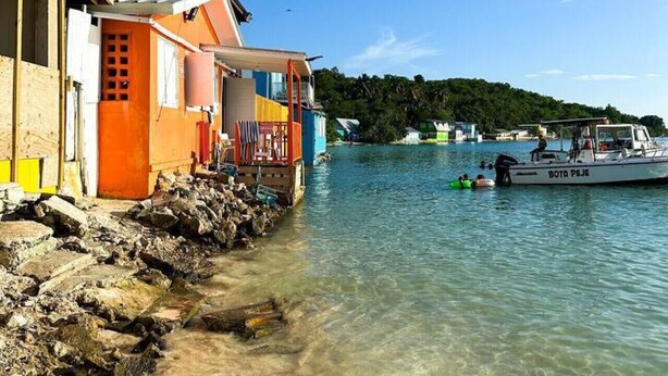 A coastal building with a clear view of the water and a boat named "BOTA PEJE" in the background.