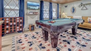 A pool table in a room with a patterned carpet, a sofa, and a television on the wall.