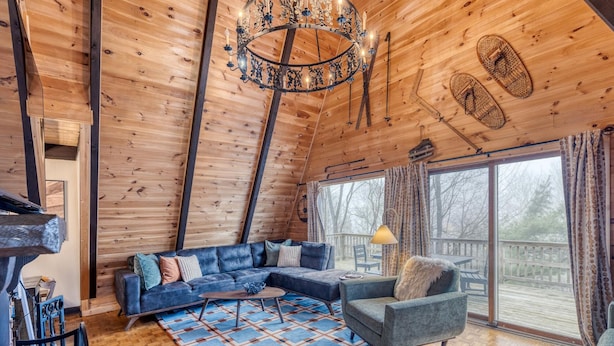 Een gezellig chaletinterieur met een houten plafond, een groot raam met uitzicht, een blauwe bank en een kroonluchter.