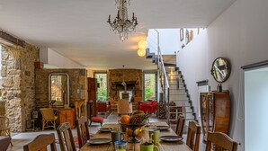 Ein Essbereich mit einem Holztisch, gedeckt für vier Personen, umgeben von Stühlen. Eine Chandelüster hängt von der Decke, und eine Treppe führt zu einer oberen Ebene.