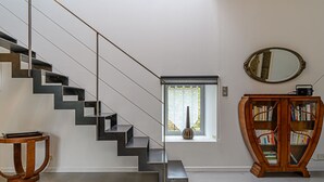 Eine moderne Treppe mit minimalistischem Design, ein kleines Fenster mit einer Vase, ein Holzregal und ein runder Spiegel an der Wand.