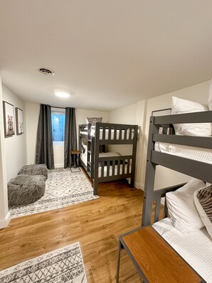 A bunk bed room with a wooden floor, a small table, and a patterned rug.
