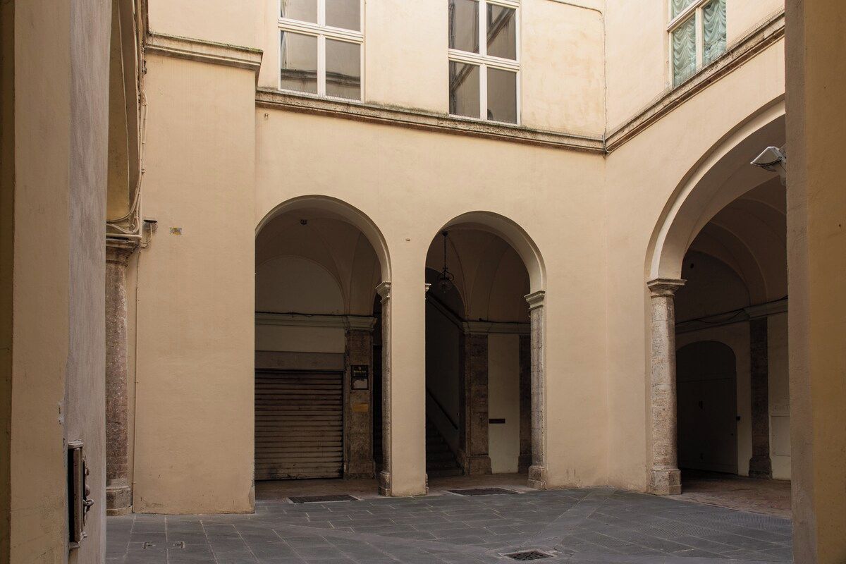 A courtyard with three arches, a closed shutter, and a staircase leading to an upper level.