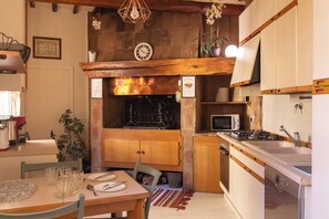 A kitchen with wooden cabinets, a microwave, a sink, and a dining area with a table set for two. - Historic Suite w/Balcony & Stunning Views in Perugia (Perugia)