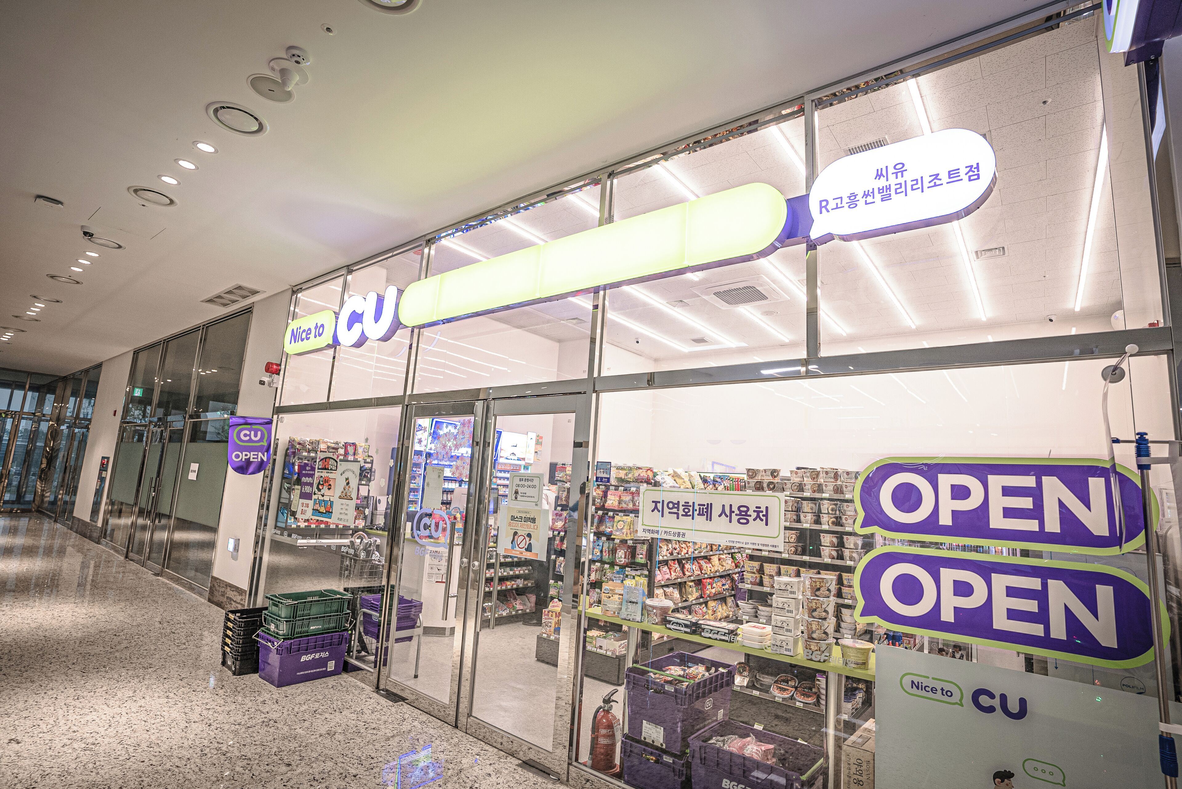 A CU store with 'OPEN' signs, glass doors, and various products on shelves.