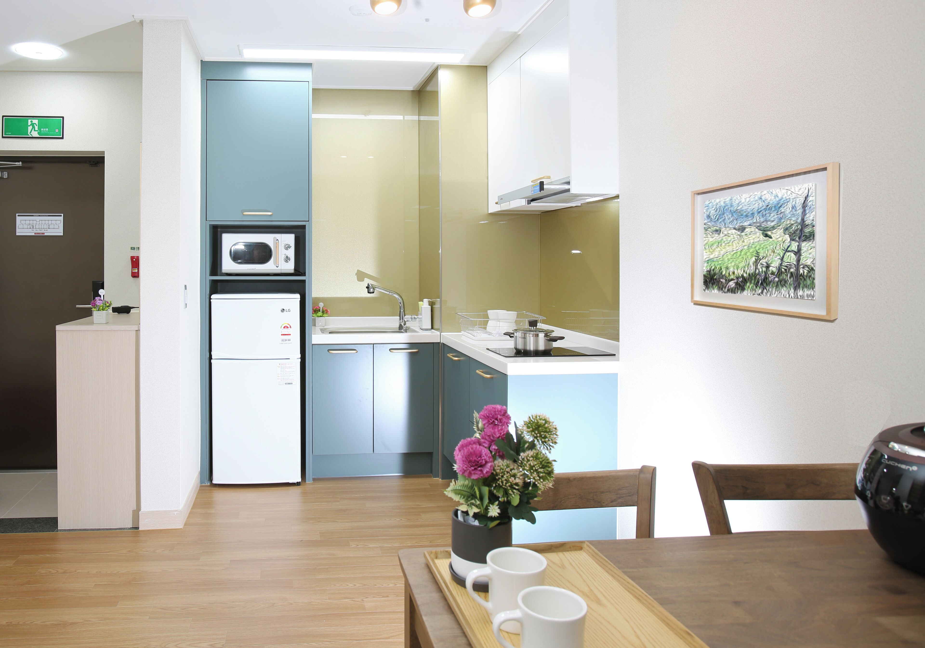 A modern kitchen with a microwave, sink, and cabinets. There is a dining table with chairs and a vase of flowers.