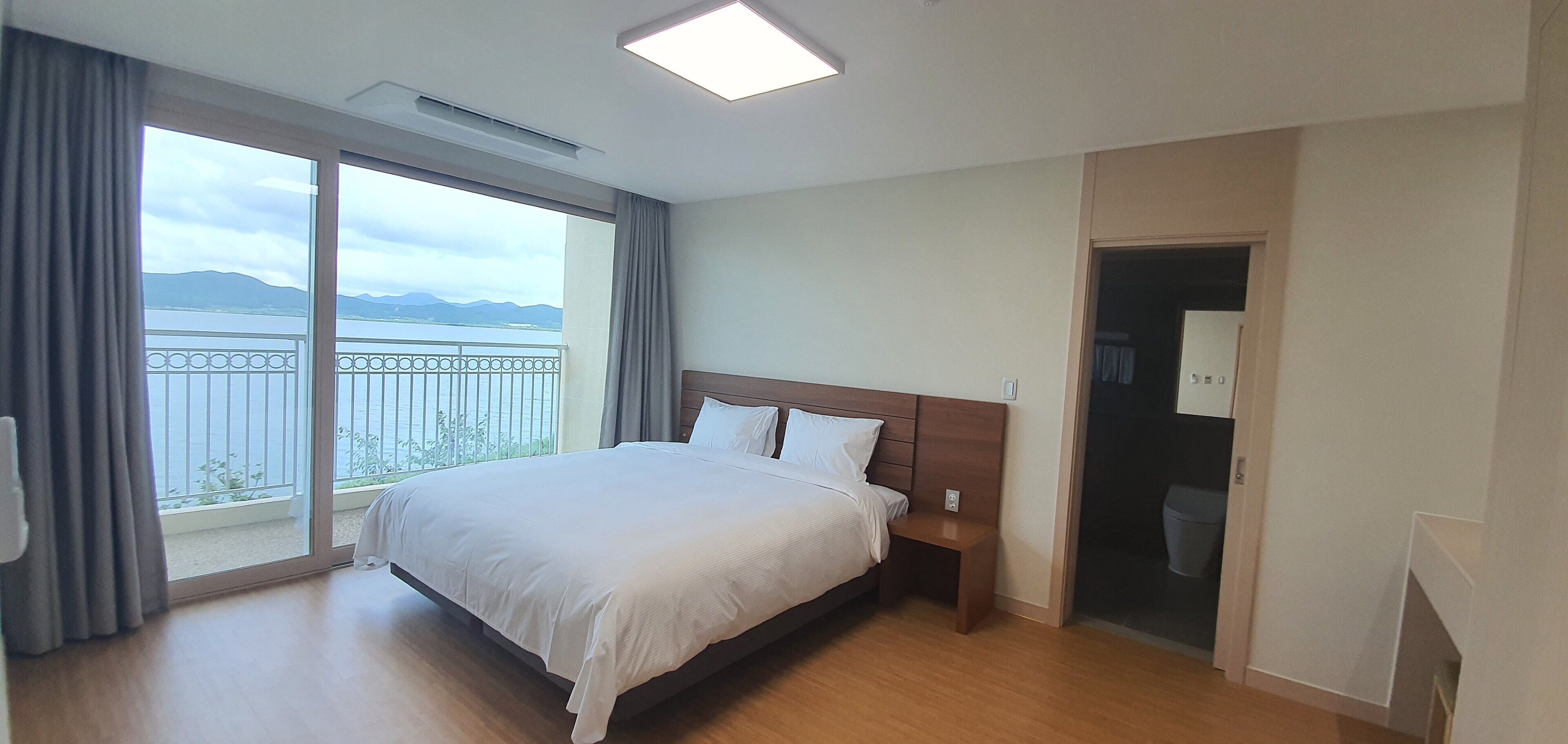 Ein Hotelzimmer mit einem großen Bett, einem Nachttisch, einem Kleiderschrank und Meerblick vom Balkon.