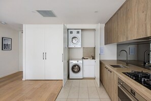A compact kitchen with a built-in washer and dryer, a sink, and a stove. - Modern, Private Luxury Apartment - Harbourside (Darlinghurst)