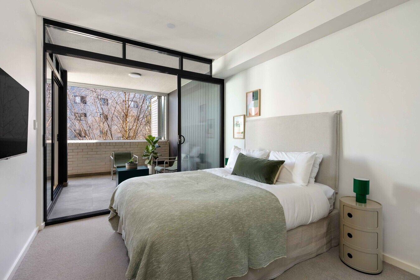 Ein modernes Schlafzimmer mit einem großen Bett, einer Schiebetür zum Balkon und einem kleinen Tisch mit Stühlen.