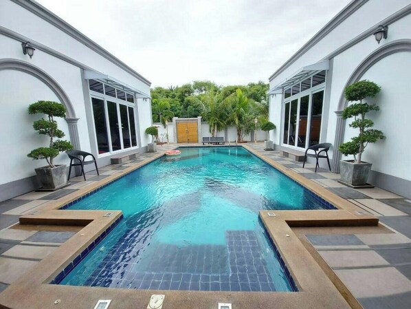 A rectangular swimming pool with a tiled edge, surrounded by a tiled deck and potted plants. - Davinci Pool Villa (Pattaya)