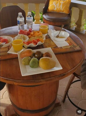 A round wooden table with breakfast items including fruits, a glass of orange juice, and a plate of pastries.