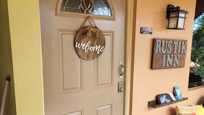 Una puerta color beige con un letrero que dice 'welcome', un letrero que indica 'Rustik Inn' y un pequeño estante con objetos.