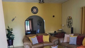 Una sala de estar con un sofá de cuero marrón, una mesa de centro de vidrio y una alfombra estampada.