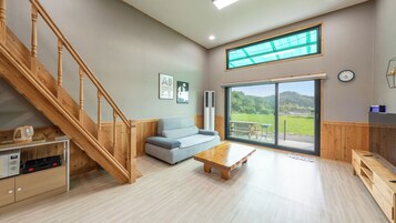 Un amplio salón con una escalera de madera, un sofá, una mesa de centro y un gran ventanal con vistas al exterior.