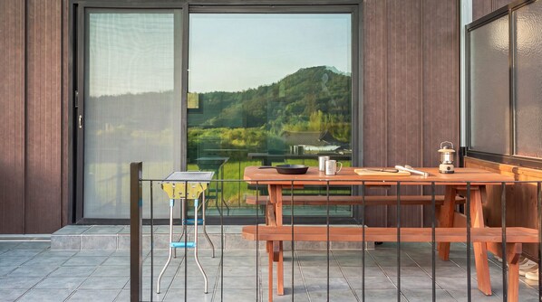 A wooden table and bench set on a balcony with a view of a green landscape.