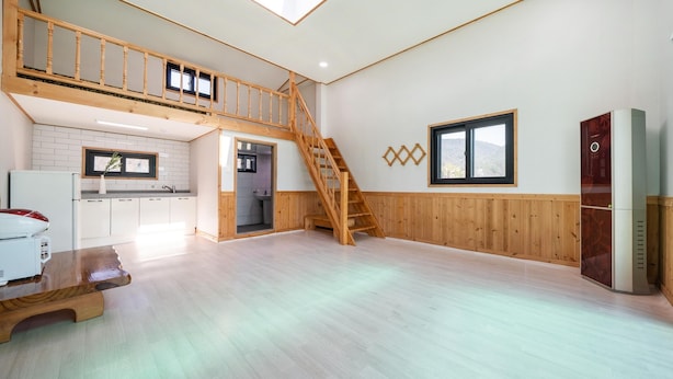 Un espacio habitable amplio con una escalera de madera, una cocina con armarios blancos y un ventanal que ofrece vistas al exterior.