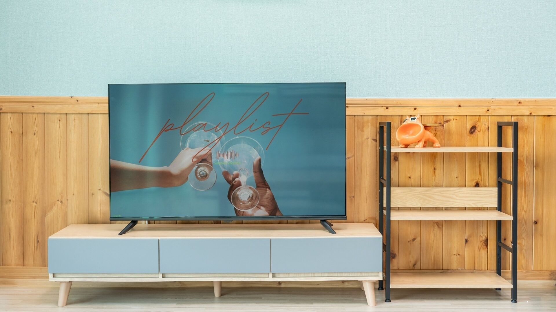 Televisor sobre un suport de fusta amb pantalla blava que mostra la paraula 'playlist' i una mà subjectant una copa de vi.