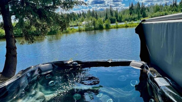 A hot tub with a clear view of a lake and surrounding trees. - Brigham Riverside Manor (Fairbanks)