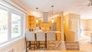 A modern kitchen with wooden cabinets, pendant lights, and a central island. - Brigham Riverside Manor (Fairbanks)