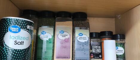 A shelf with various spice containers including iodized salt, parsley flakes, granulated garlic, black pepper, and Italian seasoning.