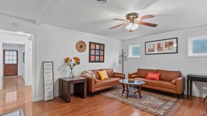A living room with a brown leather sofa, a glass coffee table, a wooden side table, a decorative rug, and a ceiling fan. - Cute ranch house -quiet & safe -3 BR  1 Bath (Imperial)