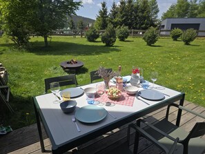 Un área de comedor al aire libre con una mesa preparada para dos personas, rodeada de césped y árboles.