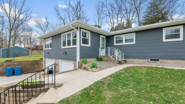 Ein zweistöckiges Haus mit Garage, einer Veranda mit Treppe und einem kleinen Vorgarten mit Rasen und einigen Blumentöpfen.