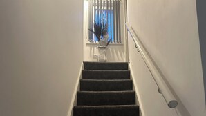 Uma escadaria com corrimão, levando a um quarto com janela e um vaso de flores.