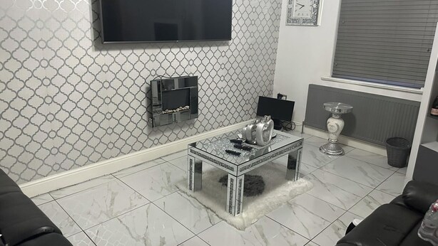 Uma sala de estar com televisão, uma mesa de centro de vidro e um vaso decorativo.