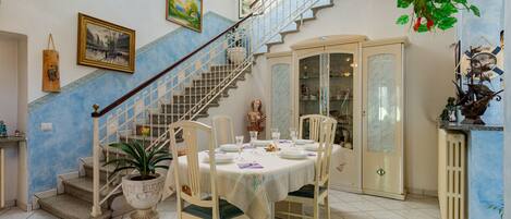 A dining area with a round table set for four, surrounded by chairs. A staircase with a wooden railing leads to an upper level.