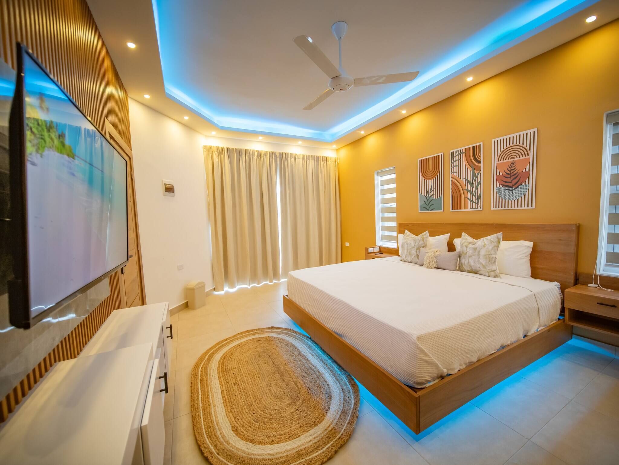 Ein modernes Schlafzimmer mit einem großen Bett, Deckenventilator, Kunstwerken und einem Flachbildfernseher.