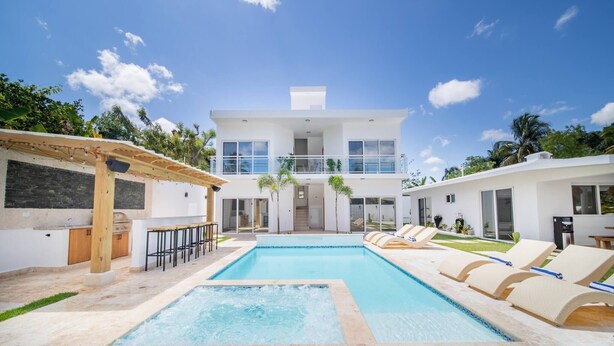 Una casa moderna de dos pisos con piscina, barra exterior y zona de estar.