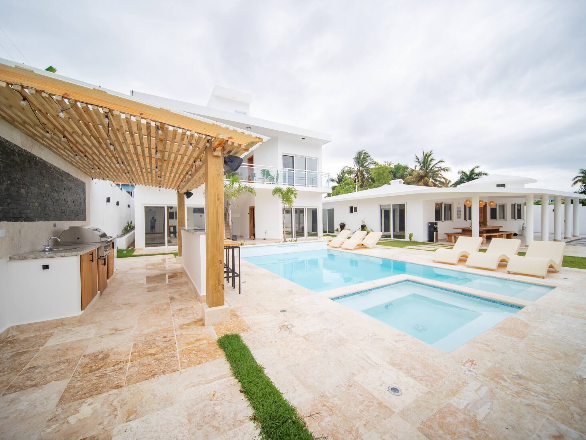 A modern outdoor pool area with a pergola, a barbecue station, and a poolside lounge with sun loungers.