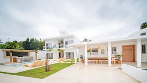 Una casa moderna de dos pisos con piscina, mobiliario de exterior y un patio cubierto.
