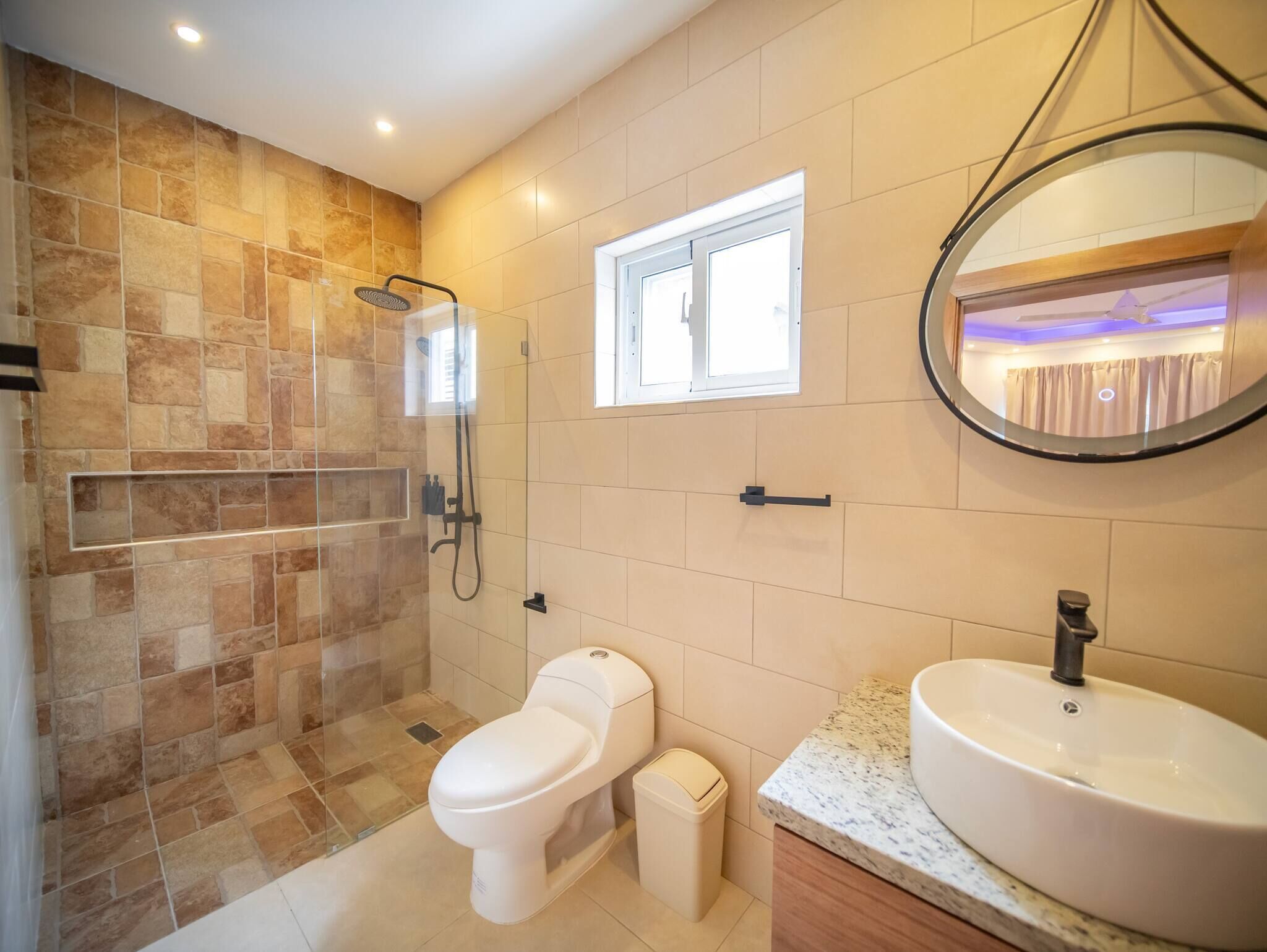 A bathroom with a shower, toilet, and sink, featuring stone tiles and a window.