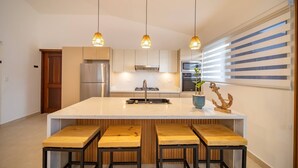 Una cocina moderna con una isla central, electrodomésticos de acero inoxidable, taburetes de madera e iluminación colgante.