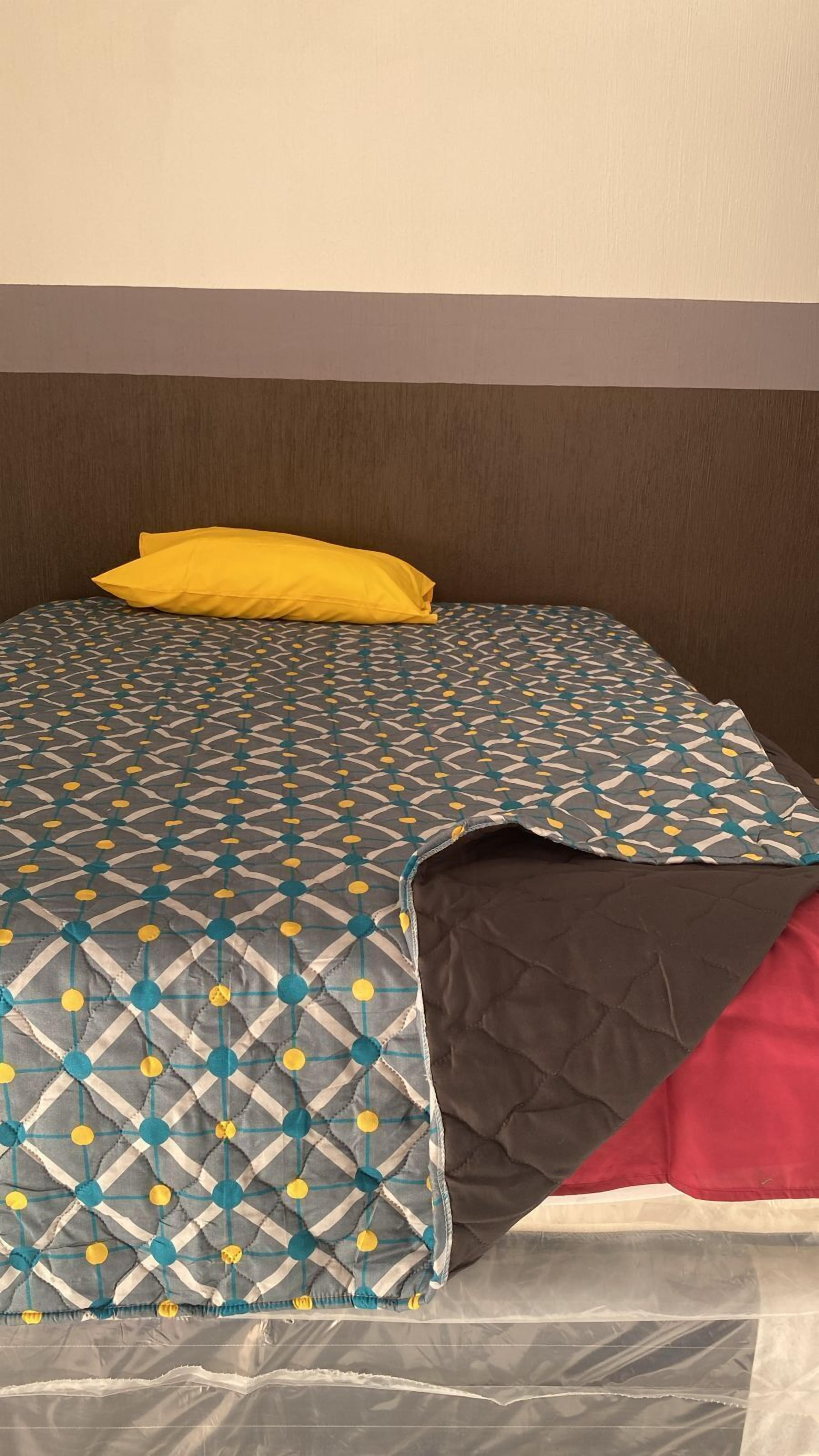 Een bed met een beddekleed met patroon, een geel kussen en een rood kussen.