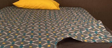 A bed with a patterned bedspread, a yellow pillow, and a red pillow.