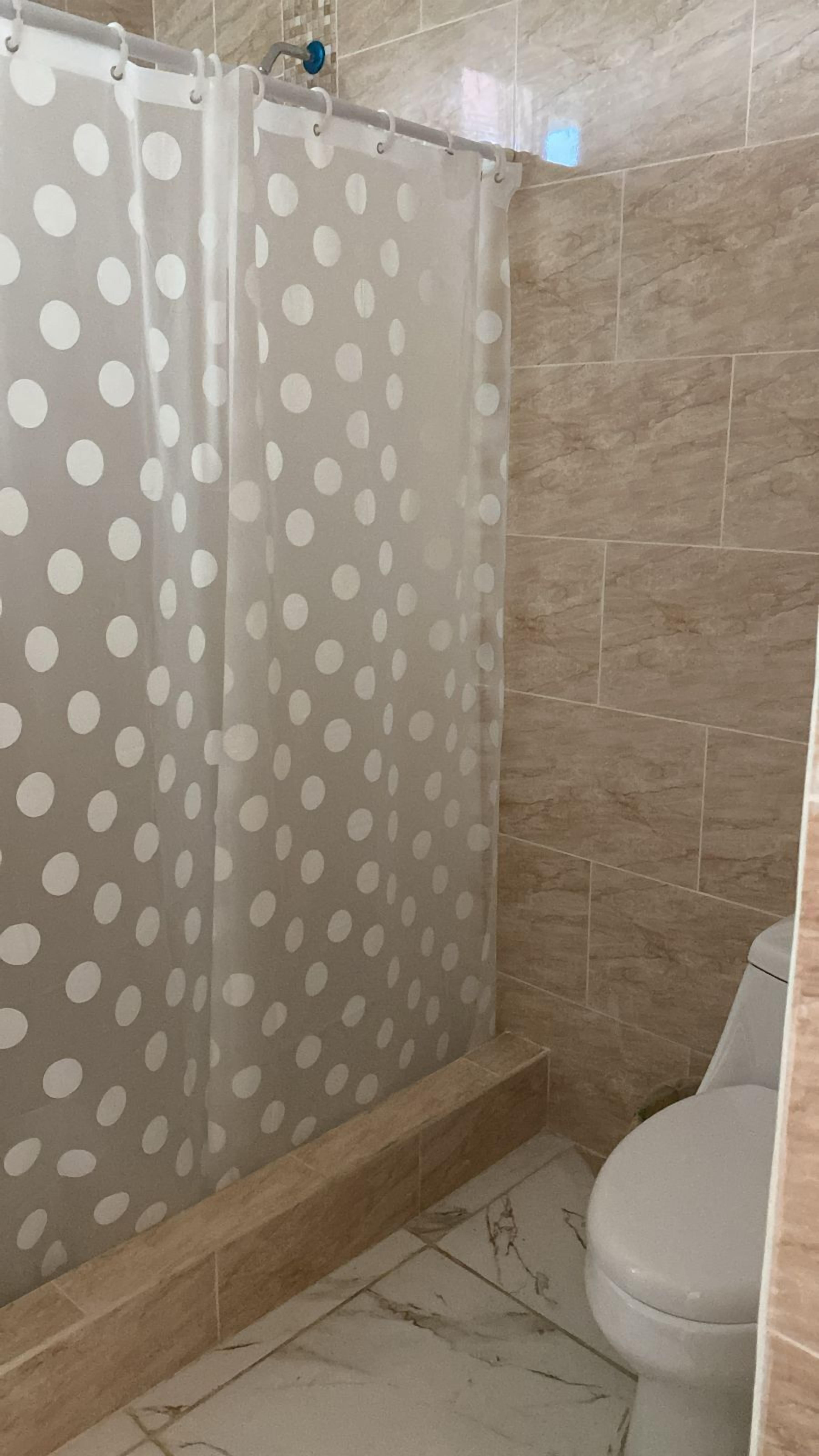 A bathroom with a shower curtain featuring a polka dot pattern, tiled walls, and a toilet.
