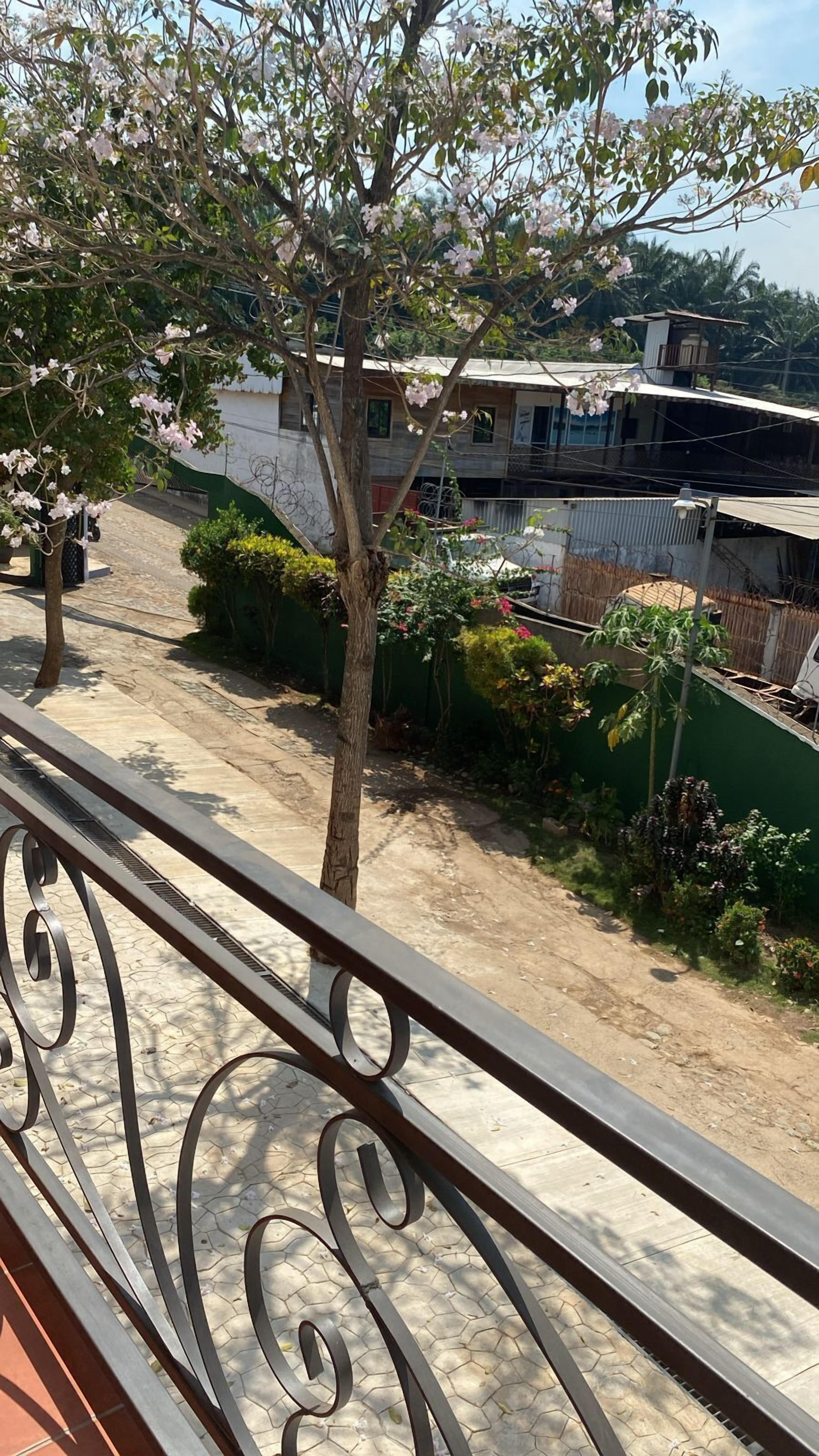 Un balcón con barandilla de metal que da a una zona residencial con árboles y un edificio.