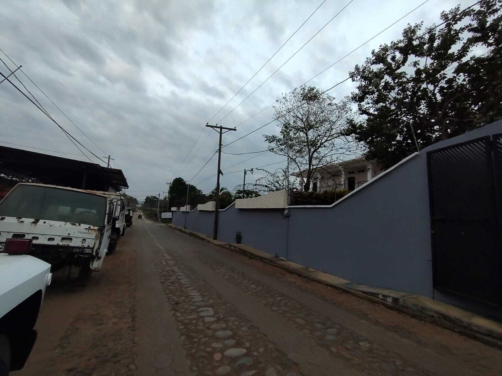 Una calle estrecha con un camión blanco estacionado a la izquierda, un muro azul a la derecha y un edificio al fondo.